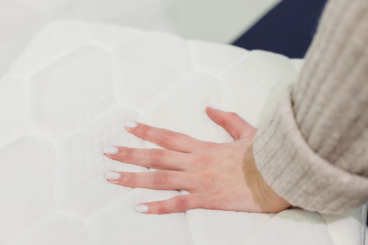 Dieses Bild zeigt eine Frauenhand, die den Härtegrad einer Matratze prüft, indem sie die Matratze eindrückt.