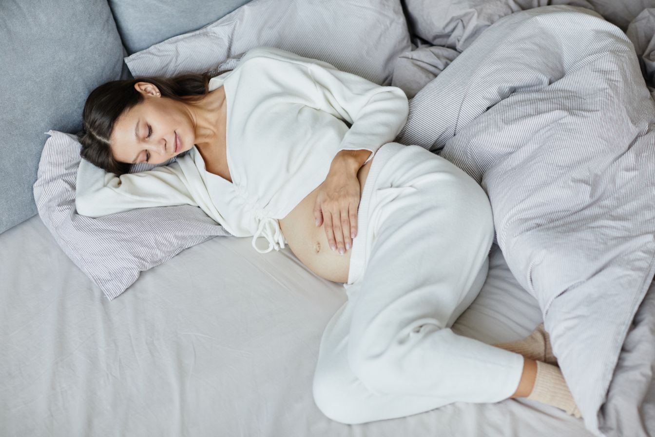 Dieses Bild zeigt eine Frau in der Schwangerschaft, die auf Ihrer Matratze liegt.